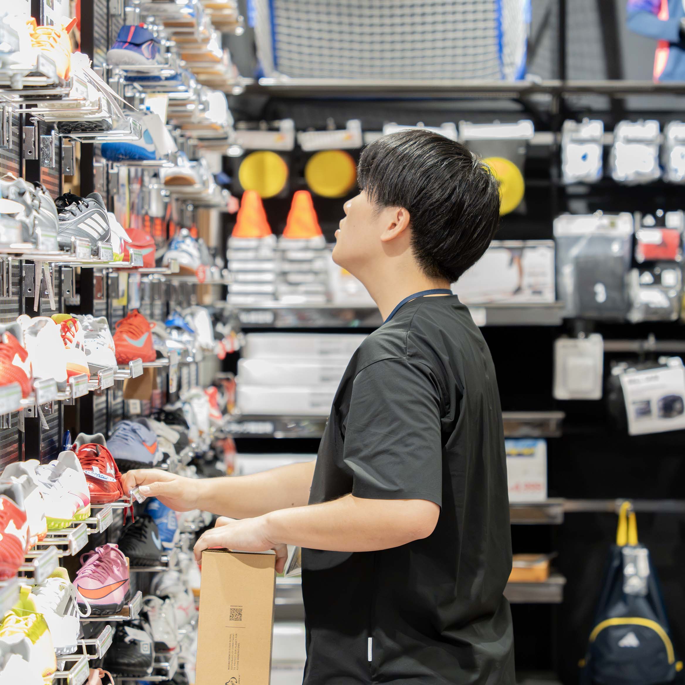 スポーツ用品店のシューズ売り場で、箱を持って商品を確認する卒業生