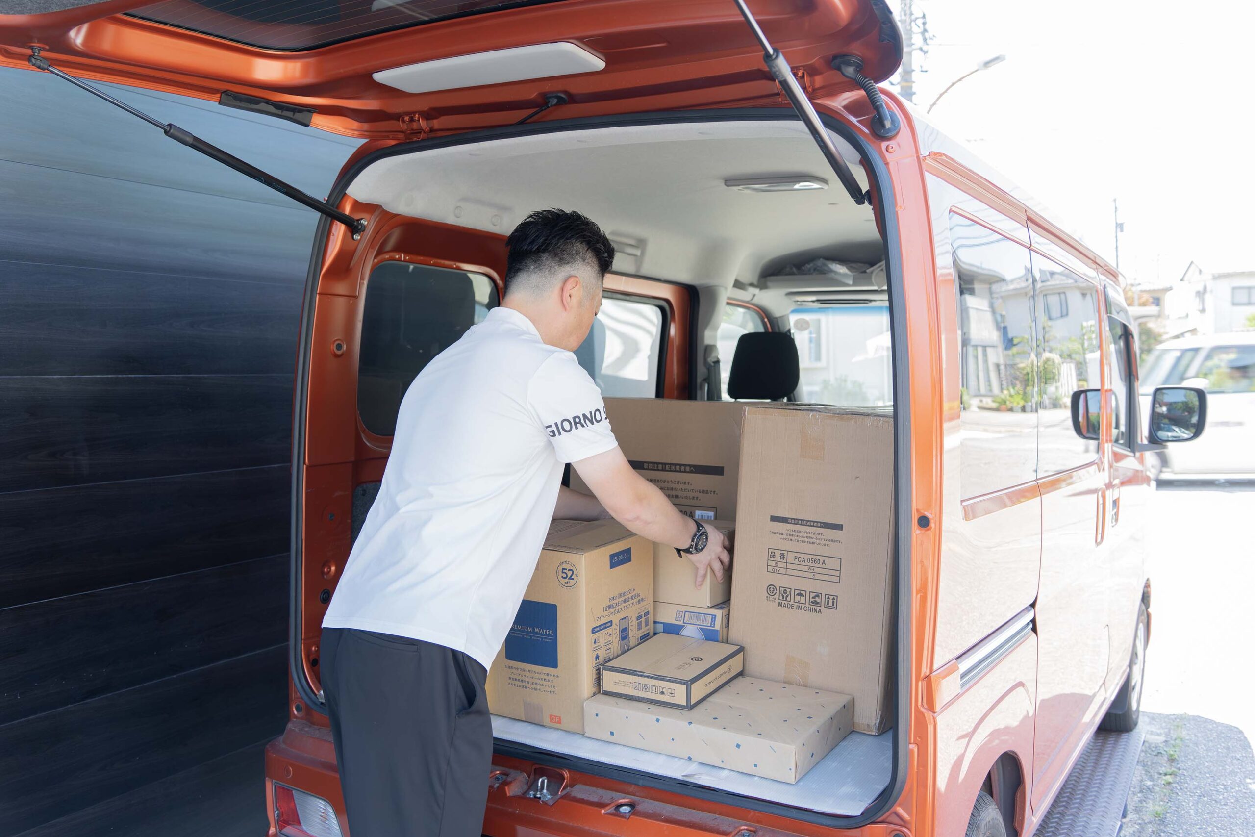 オレンジ色の配送車の荷室で、段ボールの荷物を積み込む配送スタッフ