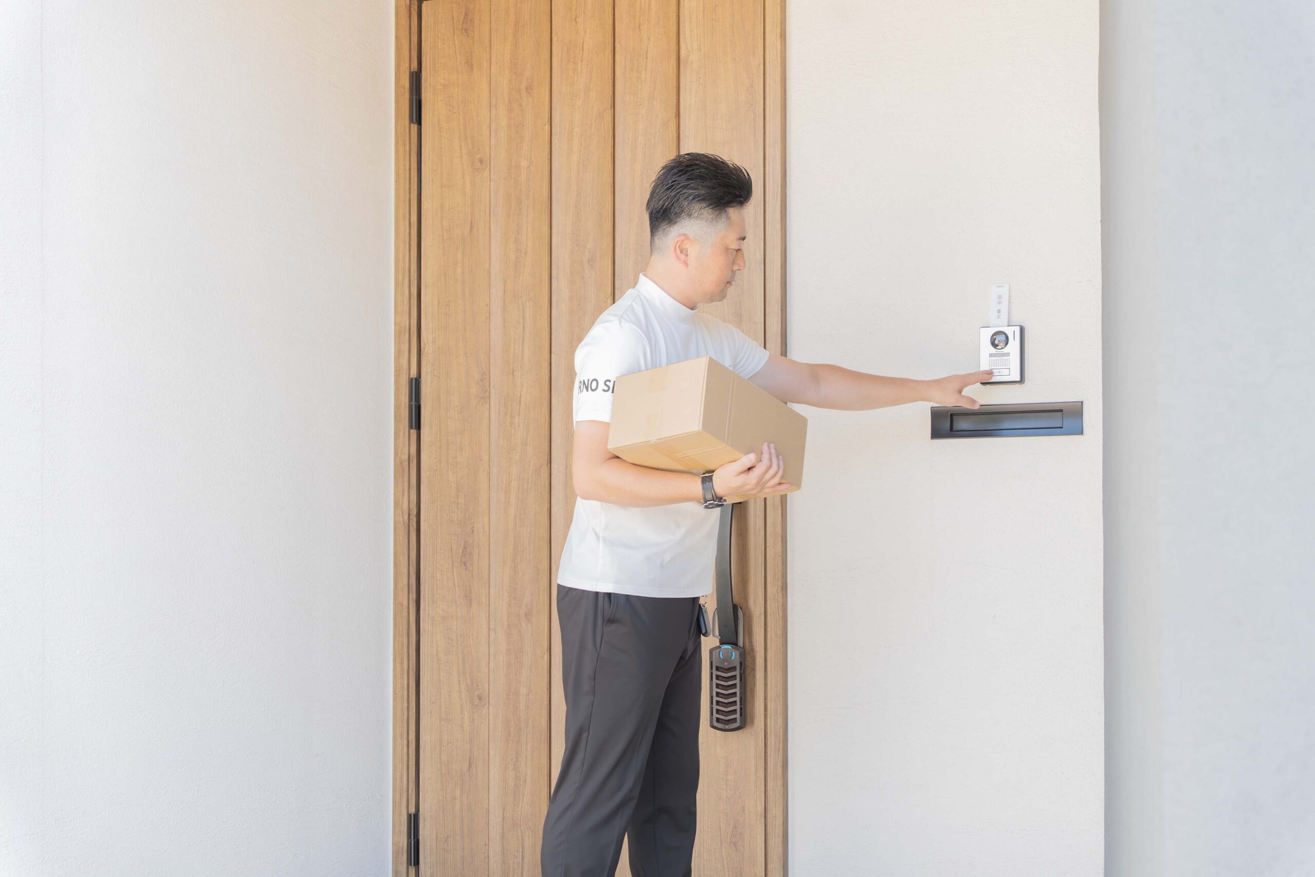 荷物を抱え、訪問先の玄関でインターホンを押す配送スタッフ