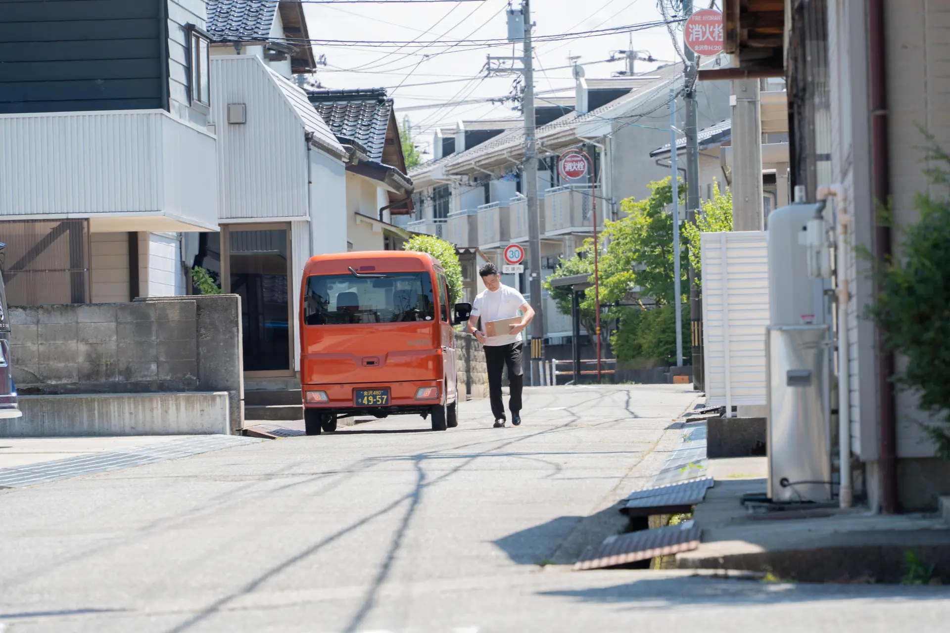 住宅街でオレンジ色の配送車から荷物を運ぶ配送スタッフ