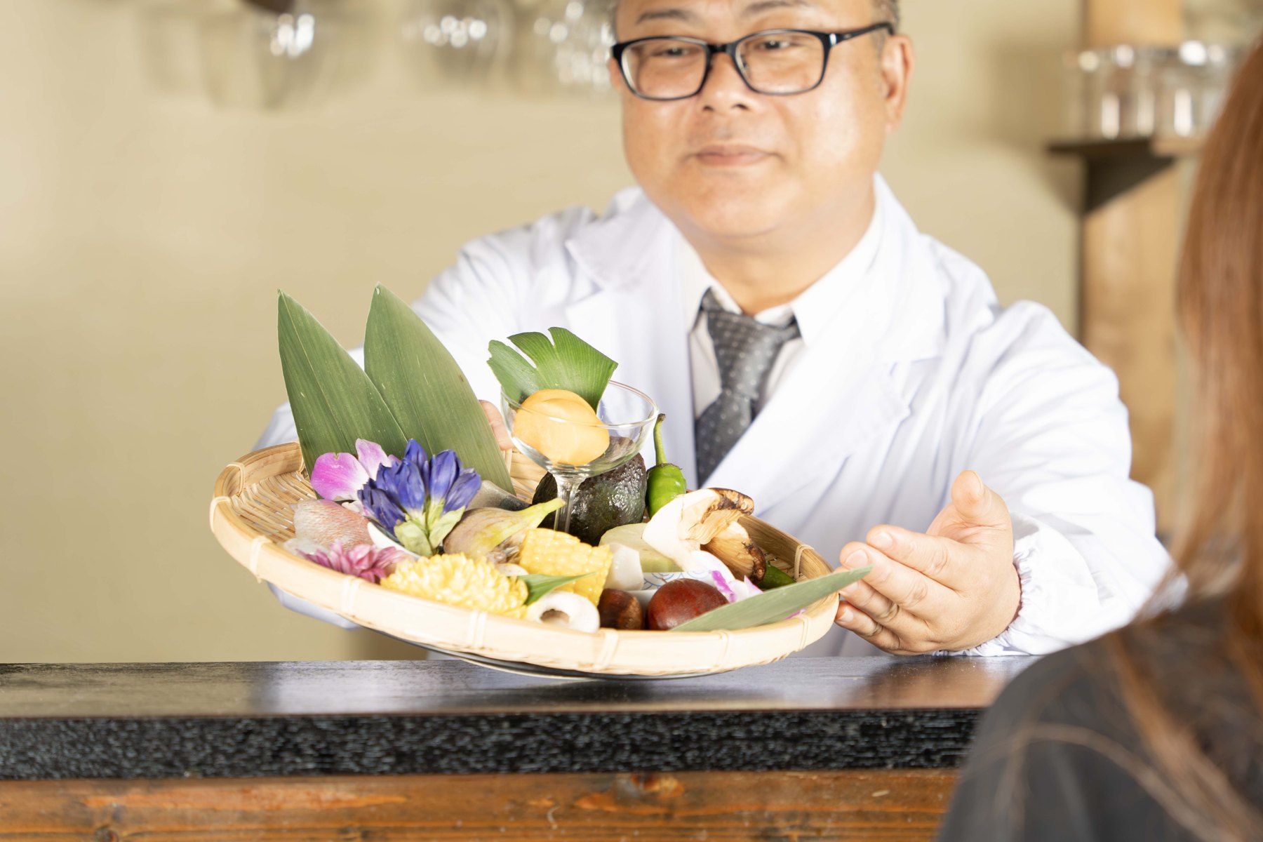 天ぷら さくの店主がカウンター越しに食材の盛り合わせを差し出す